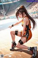 A girl in a basketball uniform crouching on a basketball court.