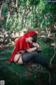 A woman in a red hooded outfit sitting on a rock in the woods.